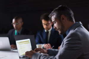 Focused man typing on laptop while working in office at night. Concentrated handsome manager sitting at table and looking at laptop. Business, working late concept